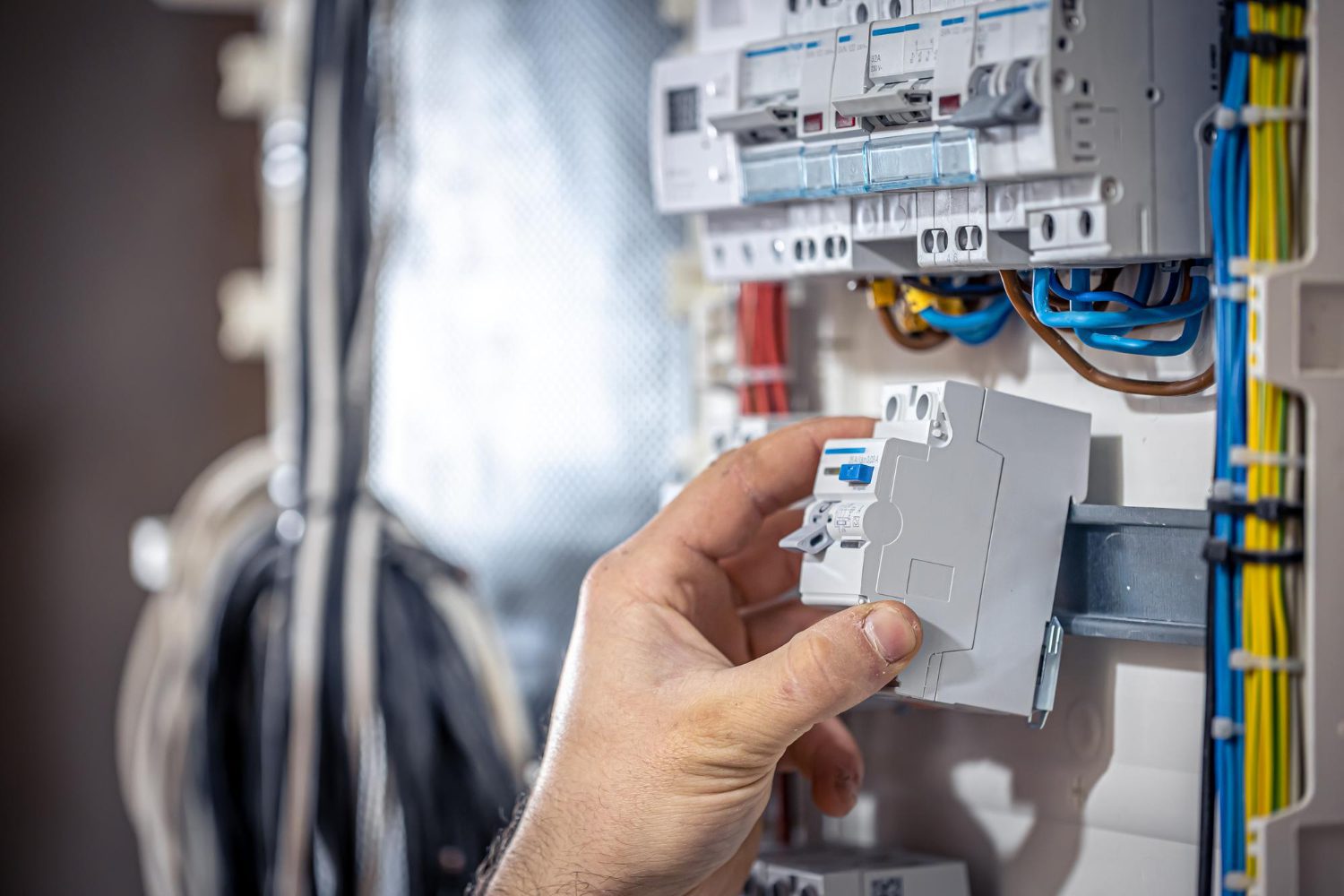 A male electrician works in a switchboard with an electrical connecting cable<br />
